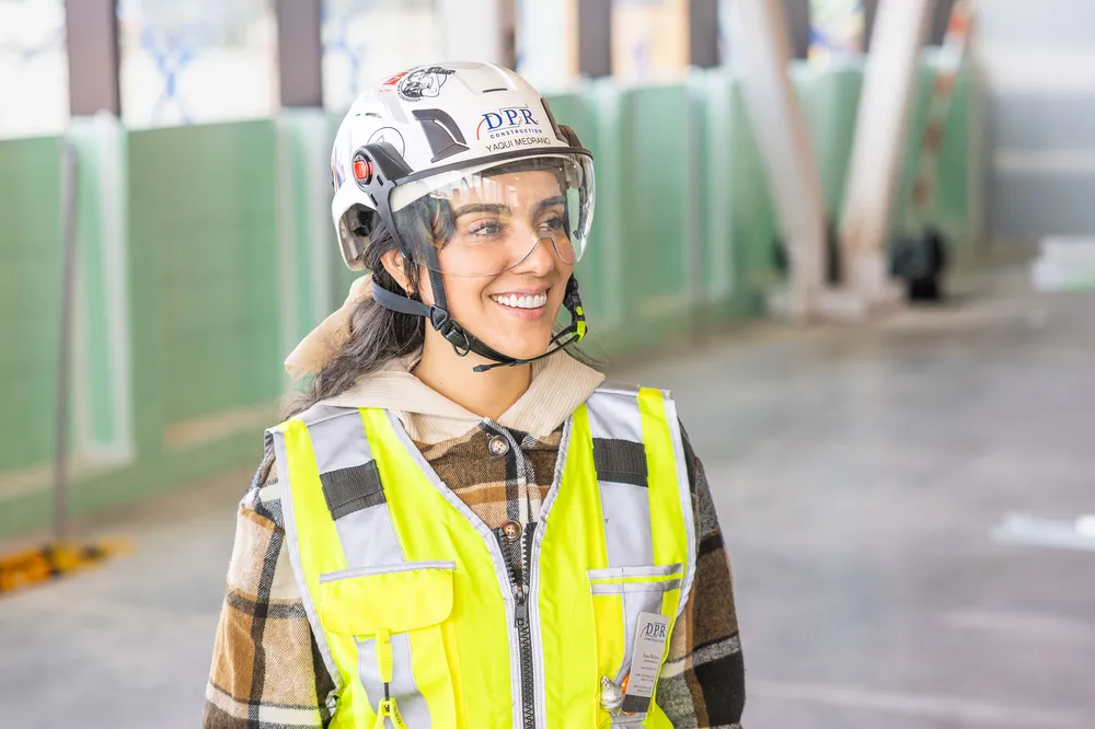 a smiling early career worker on a jobsite wearing a helmet